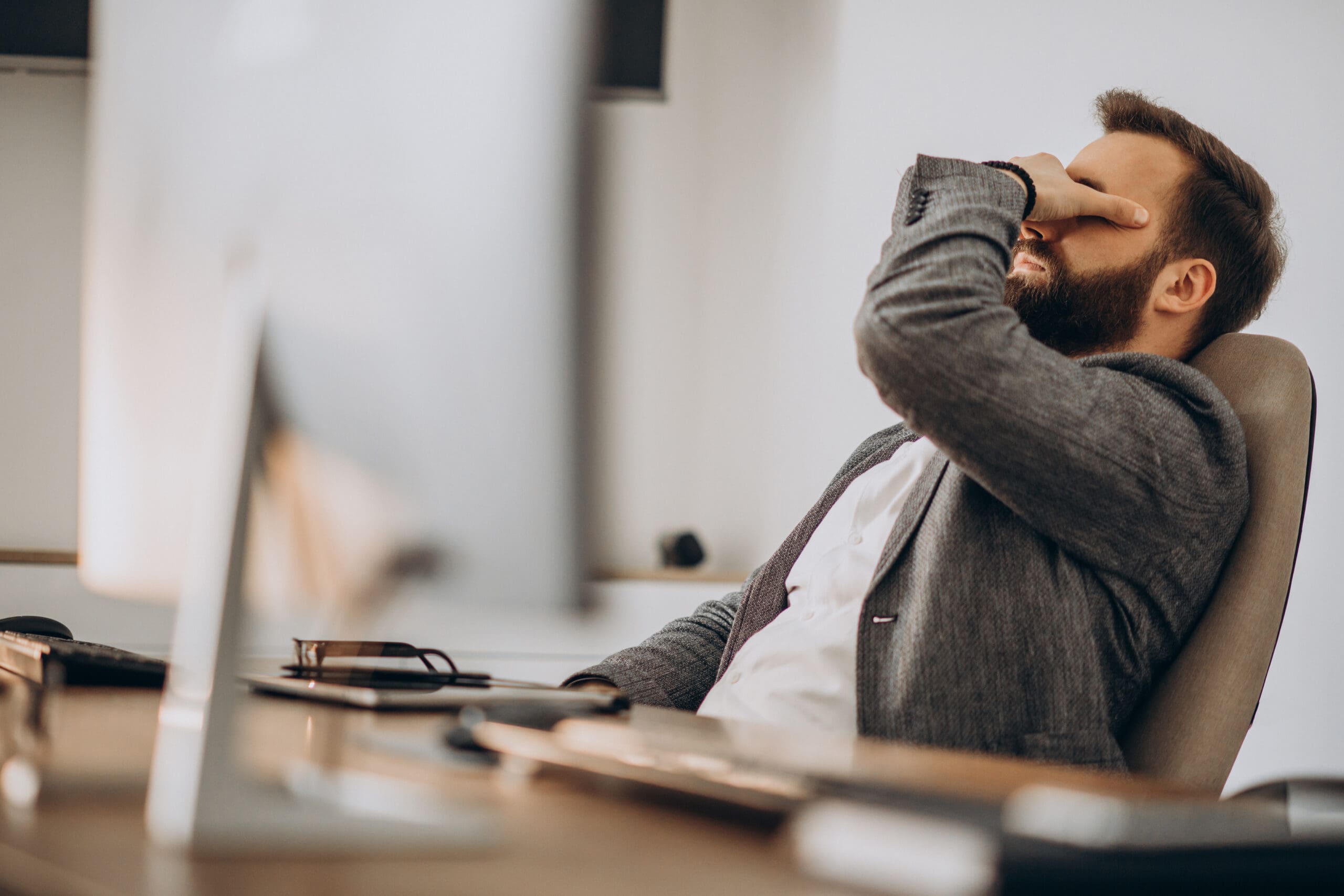 A man sitting at a desk appearing overwhelmed—illustrating signs of stress or anxiety in a work setting.